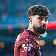 a man with curly hair and beard wearing a maroon jersey