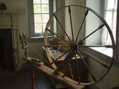 an old spinning wheel sitting in front of a window next to a table with a basket on it