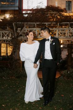 a bride and groom holding hands in front of a large building at night with lights on