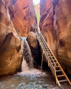 a ladder going up to a waterfall in the middle of a canyon with water running down it