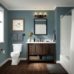 a white toilet sitting next to a sink in a bathroom under a framed painting on the wall