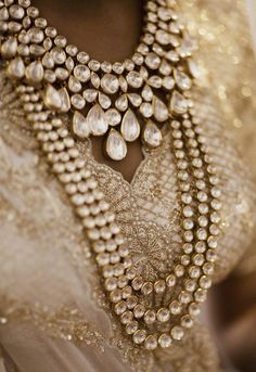 a close up of a woman wearing a gold and white outfit with jewelry on her neck