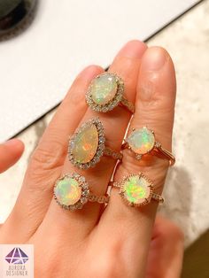 a woman's hand holding five opal rings with diamond halos on them