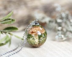 a necklace with a mushroom on it sitting next to some leaves and flowers in the background