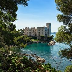 a castle sitting on top of a lush green hillside next to the ocean and trees