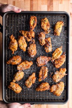 someone is holding a tray with chicken wings on it