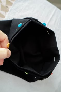 someone is stitching something in to a small black bag on top of a bed