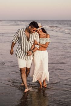 a man and woman are walking in the water at the beach with their arms around each other