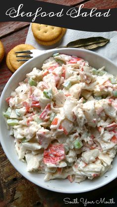 a white bowl filled with chicken salad next to crackers and a fork on the side