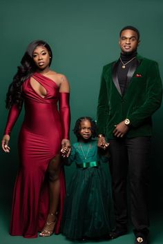 two adults and a child standing in front of a green background wearing formal wear,