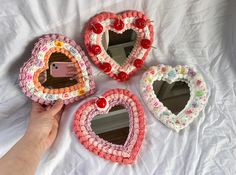 three heart shaped mirrors sitting on top of a white bed next to a person's hand