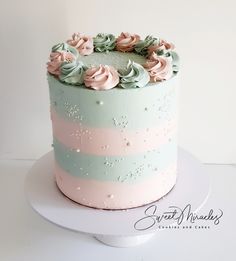 a blue and pink striped cake with frosting flowers on the top is sitting on a white plate