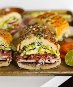 several sandwiches on a tray with limes and tomatoes