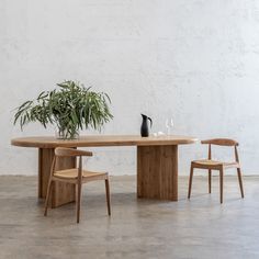 a wooden table with two chairs and a vase on the top, in front of a white wall