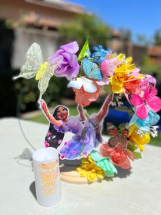 there is a paper doll with flowers on the table next to a cup and candle