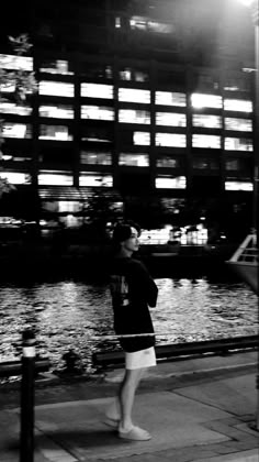 a woman standing on the sidewalk next to a body of water in front of a building