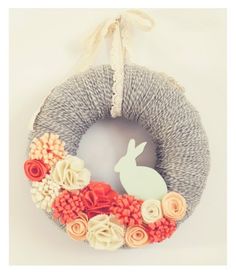 a yarn wreath decorated with flowers and a bunny on the front is hung on a wall