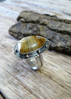 Made with a 18x24 mm natural, painted jasper cabochon, this ring reminds me of Western fields and open roads. The sandy colored gem sits on a 25x34mm base that is adorned with an unique pattern and sterling silver beads. The gem is wrapped in fine silver (.999) and sits on a sterling silver (.925) base. The stone possesses hues of chocolate brown, golden brown and black. The piece has been oxidized and lightly polished giving it great contrast and an industrial vibe. The piece is weighty and ric Unique Jasper Ring Jewelry, Artisan Jasper Jewelry In Oval Shape, Artisan Oval Jasper Jewelry, Oval Jasper Cabochon Jewelry, Unique Jasper Rings For Gift, Oval Cabochon Jasper Jewelry, Artisan Brown Gemstone Rings, Bohemian Agate Ring With Large Stone, Artisan Agate Cabochon Rings