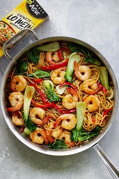 a wok filled with shrimp and noodles next to a carton of pasta sauce