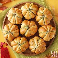 a wooden plate topped with rolls on top of a green cloth next to autumn leaves