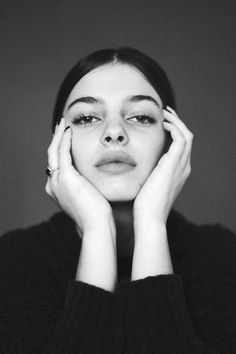 a black and white photo of a woman with her hands on her face, looking at the camera