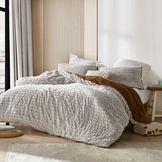 a bed sitting in a bedroom next to a window with lots of pillows on top of it