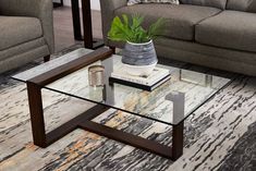 a glass table with a plant on top in front of a couch and coffee table