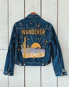 a denim jacket with the words wanderr on it hanging from a wooden wall next to a cactus