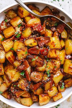 a white bowl filled with cooked potatoes on top of a marble counter next to a spoon