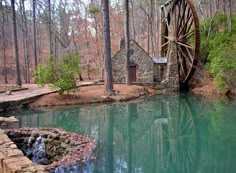 a water mill in the middle of a forest with blue water and trees around it