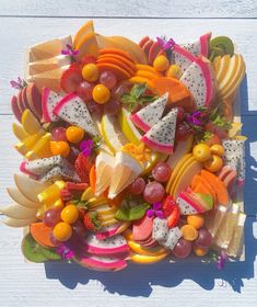 a platter filled with lots of fruit on top of a white wooden table next to a shadow