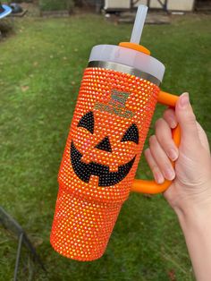 a hand holding an orange cup with a pumpkin face on it