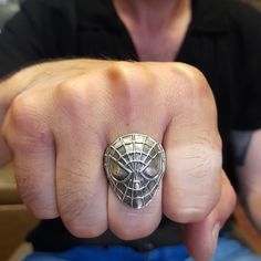 a man wearing a silver ring with a spiderman mask on it's middle finger