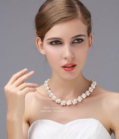 a woman in a white dress wearing a necklace with pearls on the neck and shoulder