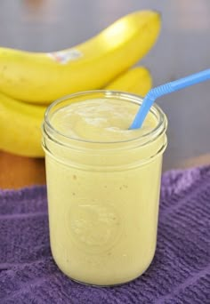 a glass jar filled with yellow smoothie next to two bananas on a purple towel