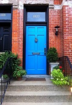 a blue door is on the side of a red brick building with black railings