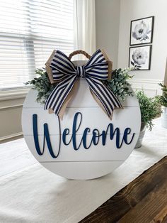 a welcome sign with a bow on it sitting on top of a table next to a potted plant