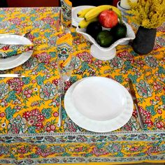 the table is set with white plates, silverware and fruit in vases on it