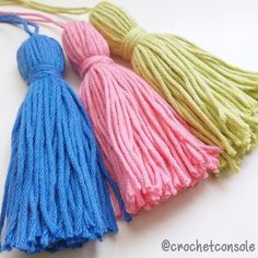 three yarn tassels are shown on a white surface, one is blue and the other is pink