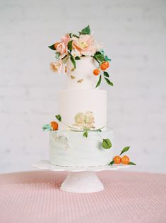 a three tiered white cake with flowers on the top and bottom, sitting on a pink tablecloth