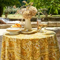 the table is set for two outside with flowers and fruit in vases on it