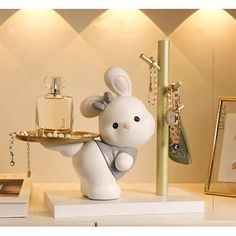 a white rabbit figurine holding a tray with jewelry on it's feet