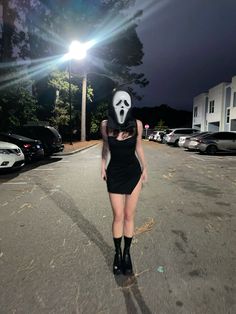 a woman in a black dress and mask walking down the street