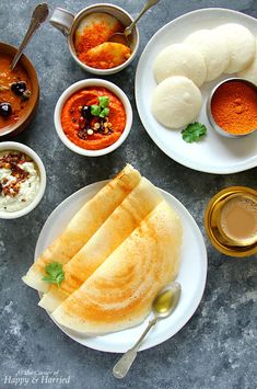 an assortment of food on plates with spoons and sauces around them, including pita bread