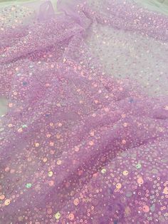 purple and pink sequins are scattered on a sheet that is laying on the floor