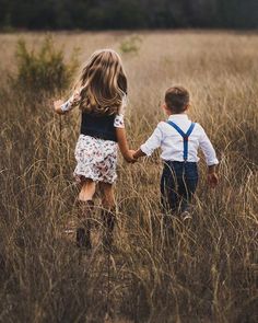 a little boy and girl holding hands while walking through tall grass