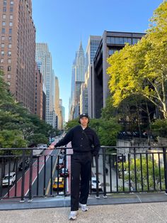 a man standing on the side of a road in front of tall buildings and trees