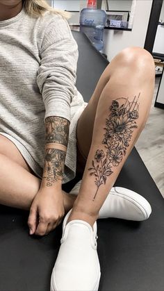 a woman sitting on top of a table with her legs crossed and flowers tattooed on the leg