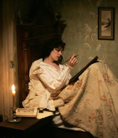 a woman sitting on top of a bed next to a book and candle in her hand