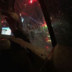 a person sitting in the passenger seat of a car on a rainy night with red and green lights